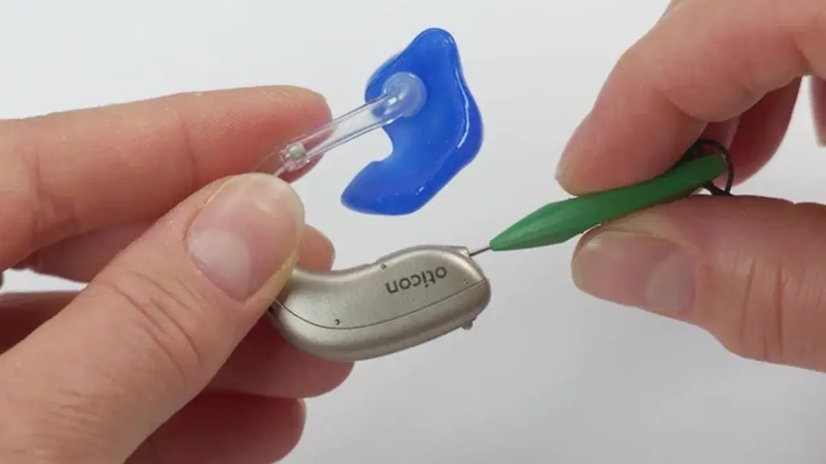 Hands replacing wax guard on Oticon hearing aid device