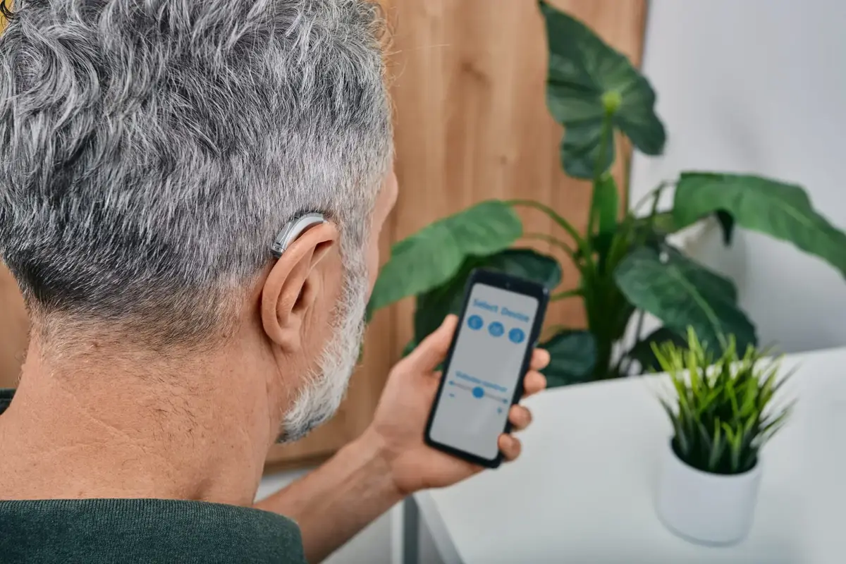 Senior man adjusting hearing aid using smartphone app