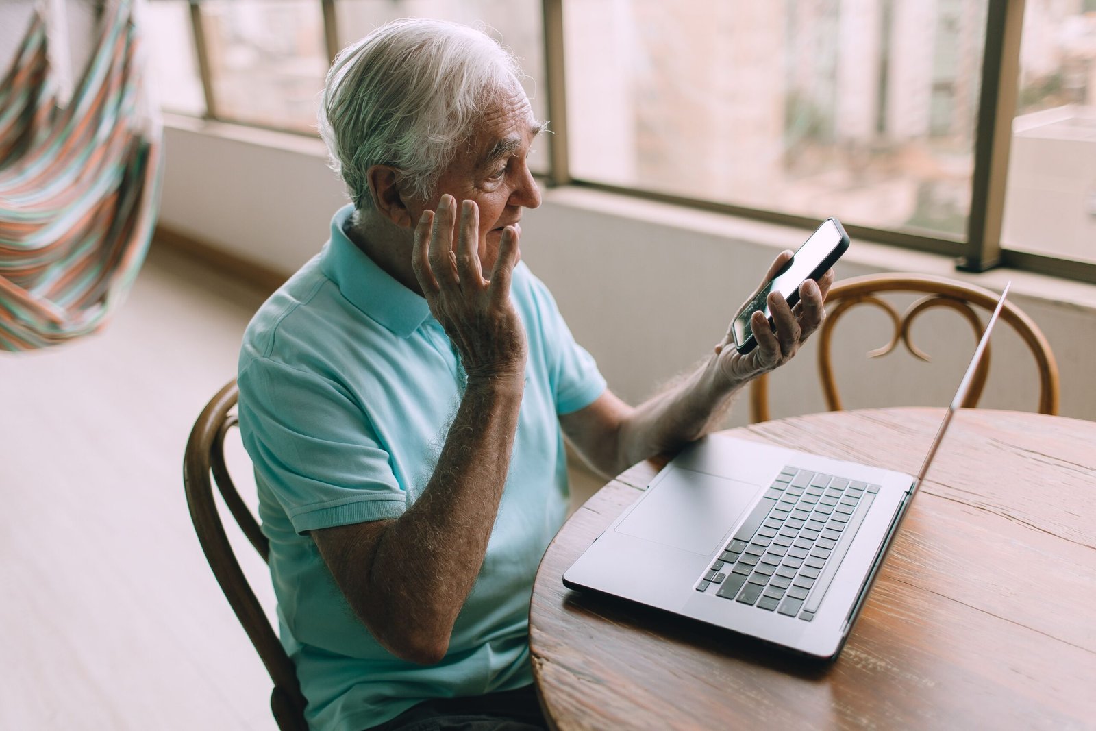 Elderly man troubleshooting smartphone and laptop